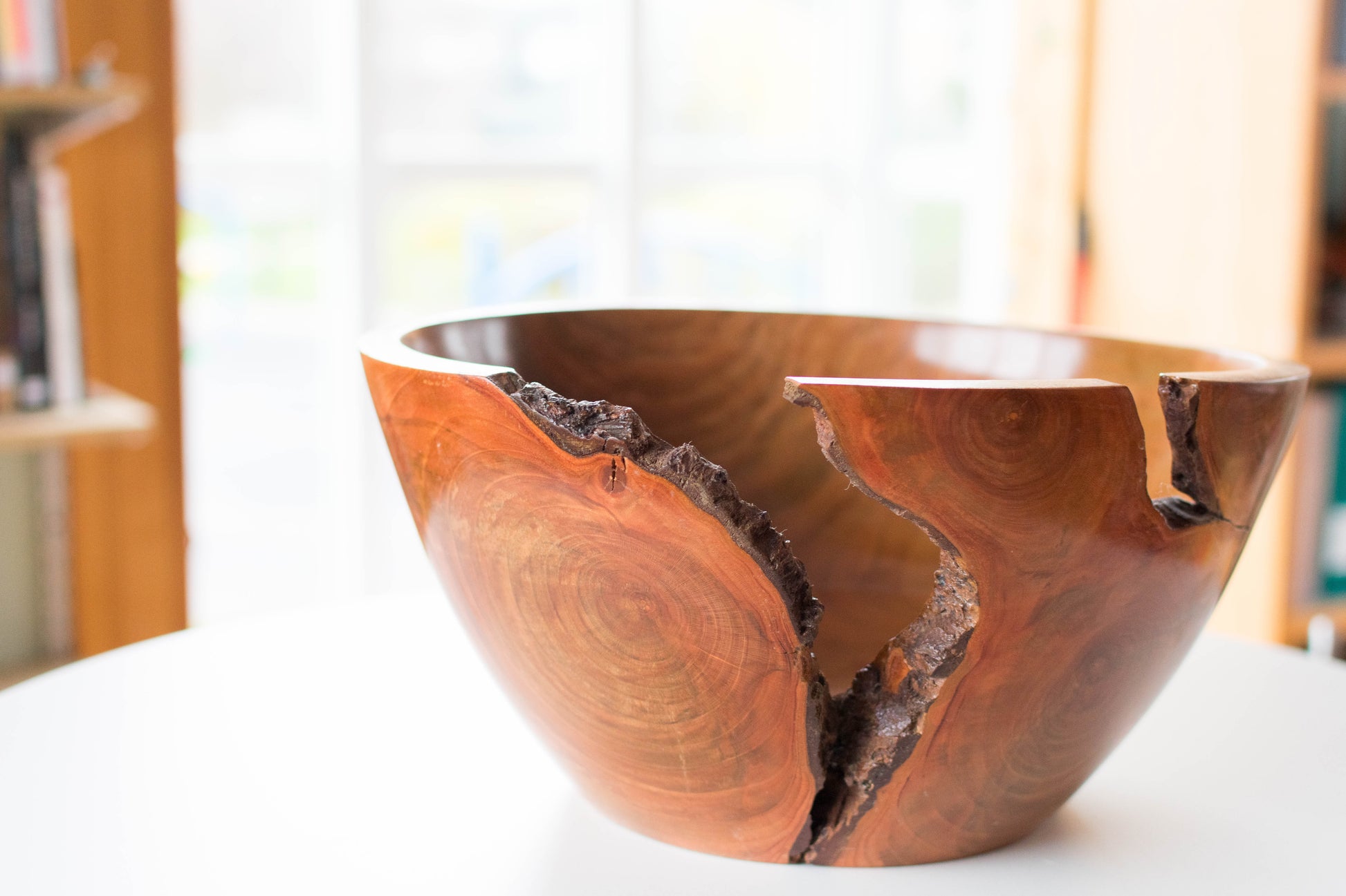 A wooden bowl with a natural crack, showing wood grain and a polished finish, sitting on a white surface.