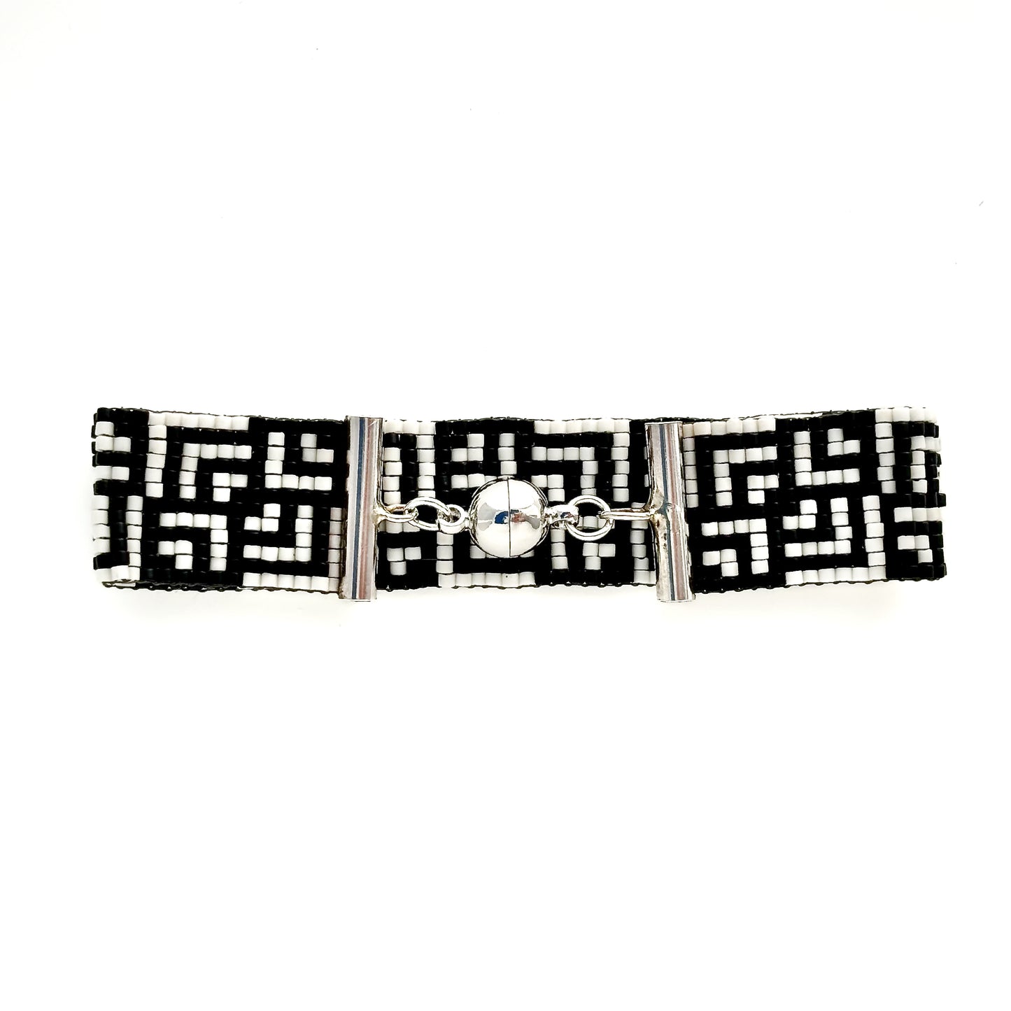 A flat lay shows a beaded bracelet with a black and white Greek key pattern and a silver magnetic clasp.