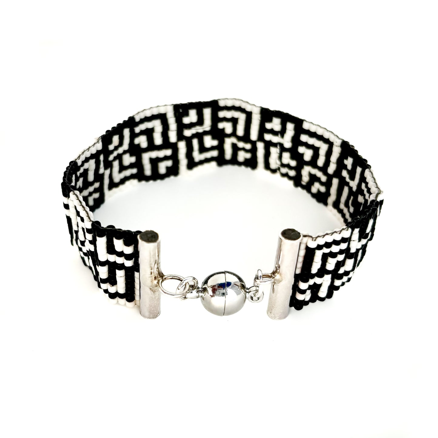 A beaded bracelet with a black and white Greek key peyote pattern features a silver magnetic clasp.