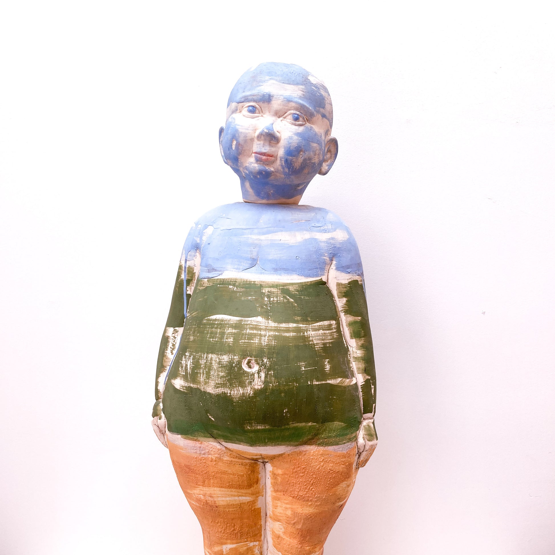 A full shot of a baby sculpture with a blue-painted face and a green and brown torso.