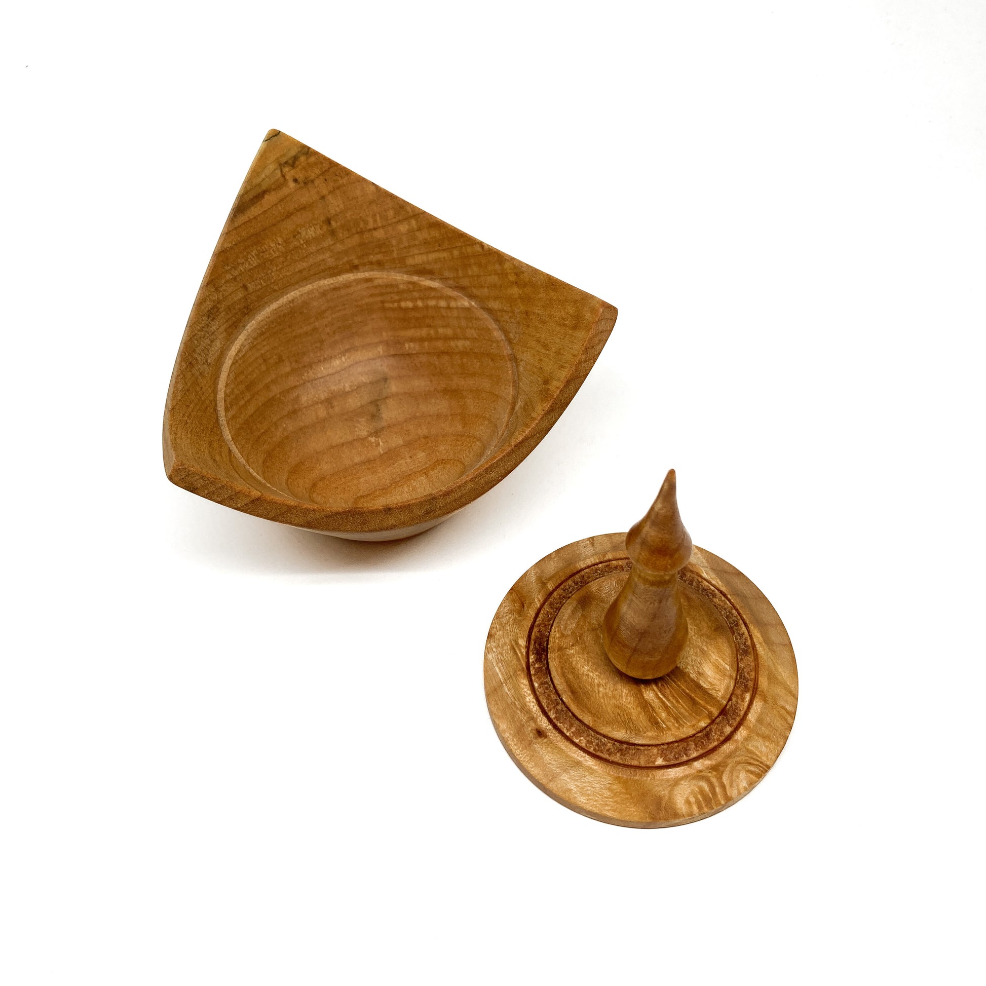 A turned wooden box with a pointed finial on the lid, with the lid removed.