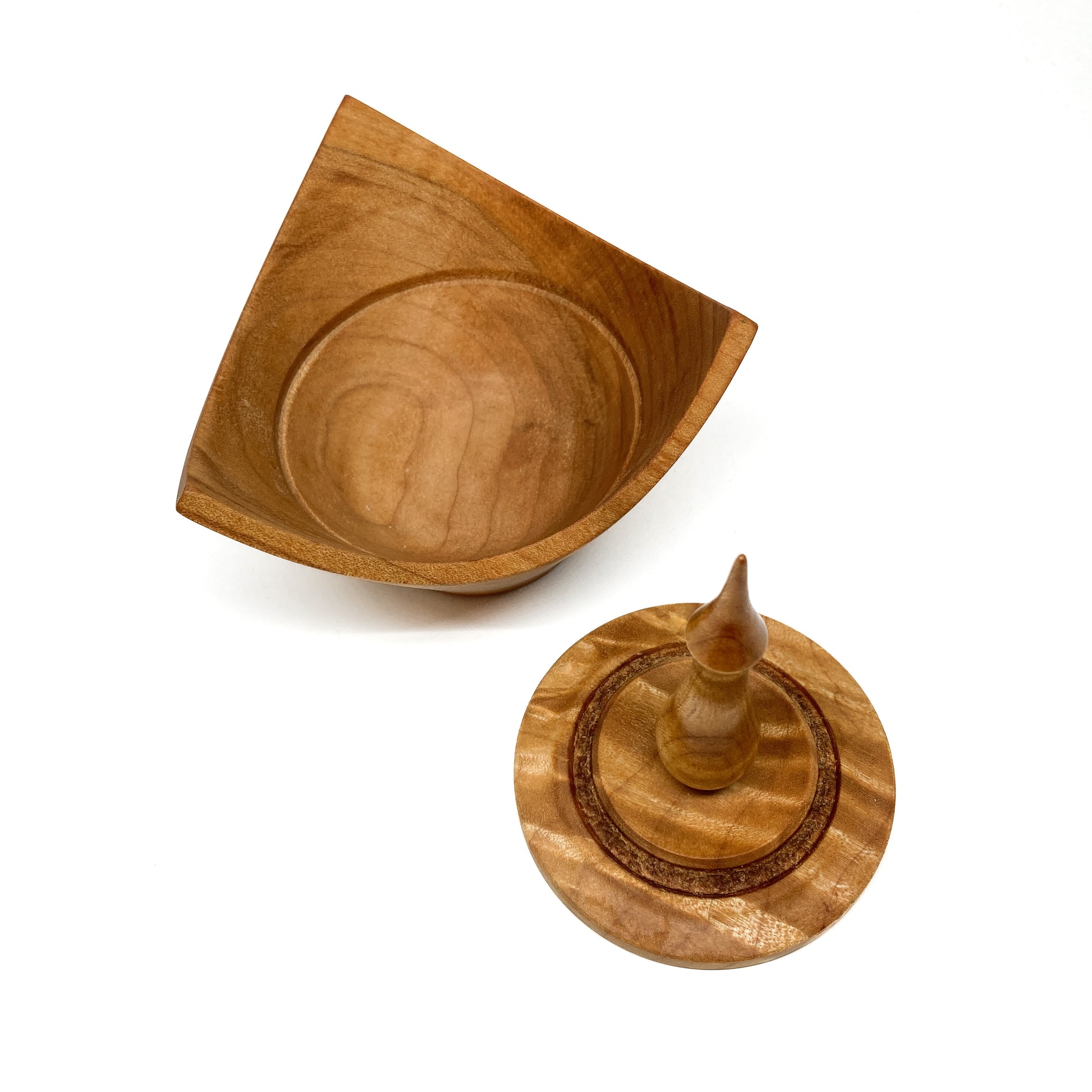 A turned wooden box with a pointed finial on the lid, with the lid removed.