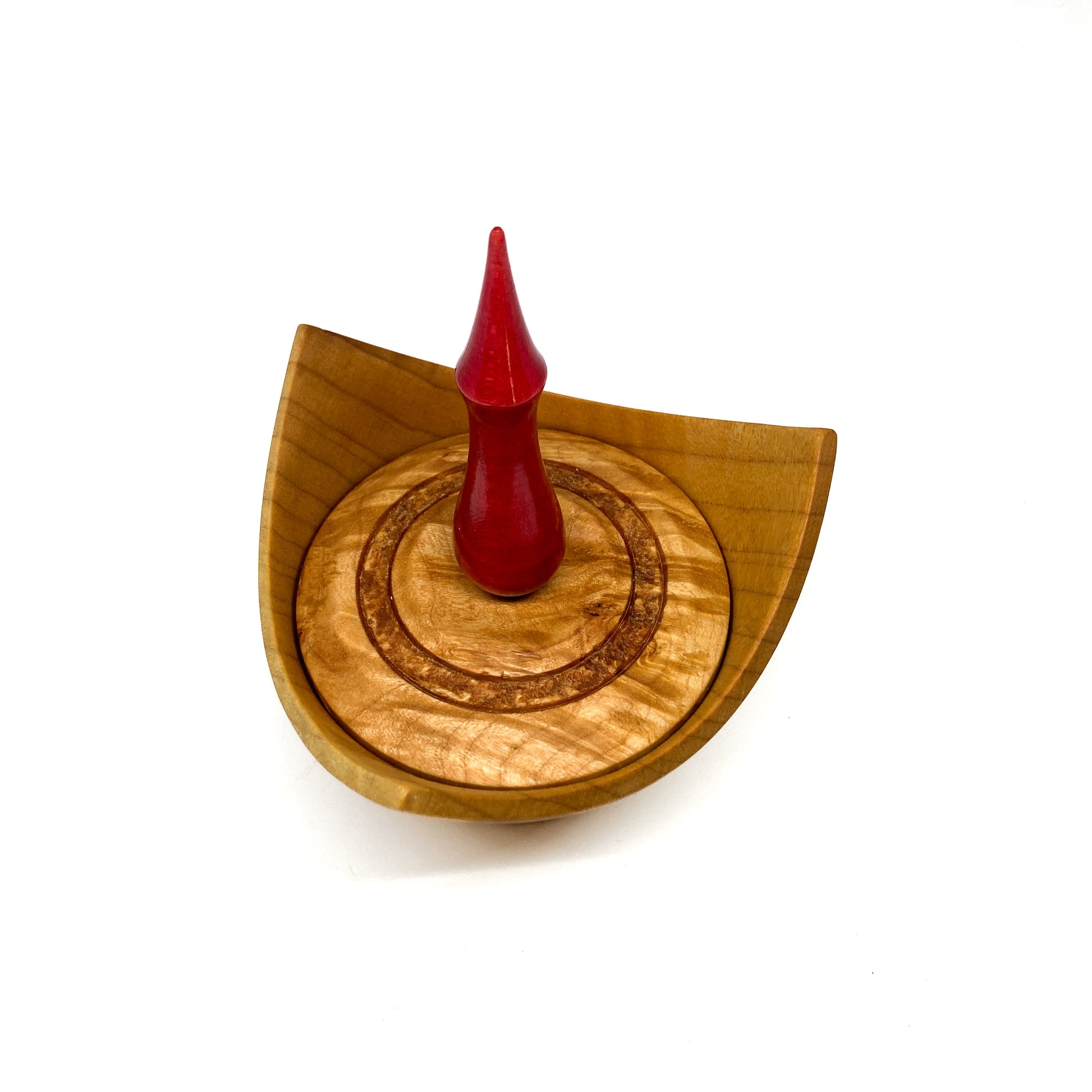 A turned wooden box with a pointed red finial on the lid, viewed from above.
