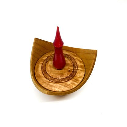 A turned wooden box with a pointed red finial on the lid, viewed from above.