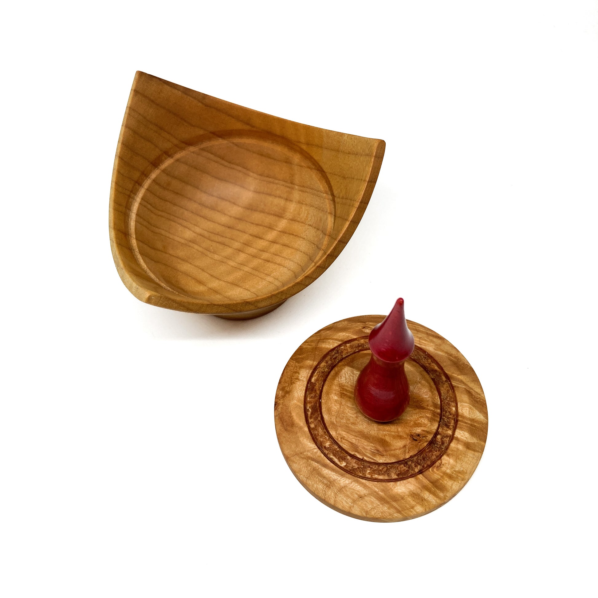 A turned wooden box with a pointed red finial on the lid, with the lid removed.