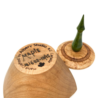 A turned wooden box lid with a pointed green finial, showing the maker's mark on the bottom.