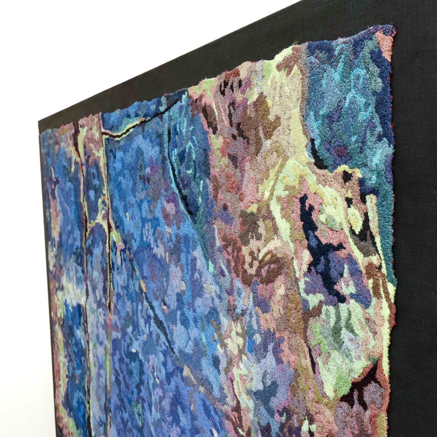 Angled view of a framed thread painting, showcasing dense stitching and colorful thread in a textured embroidery.