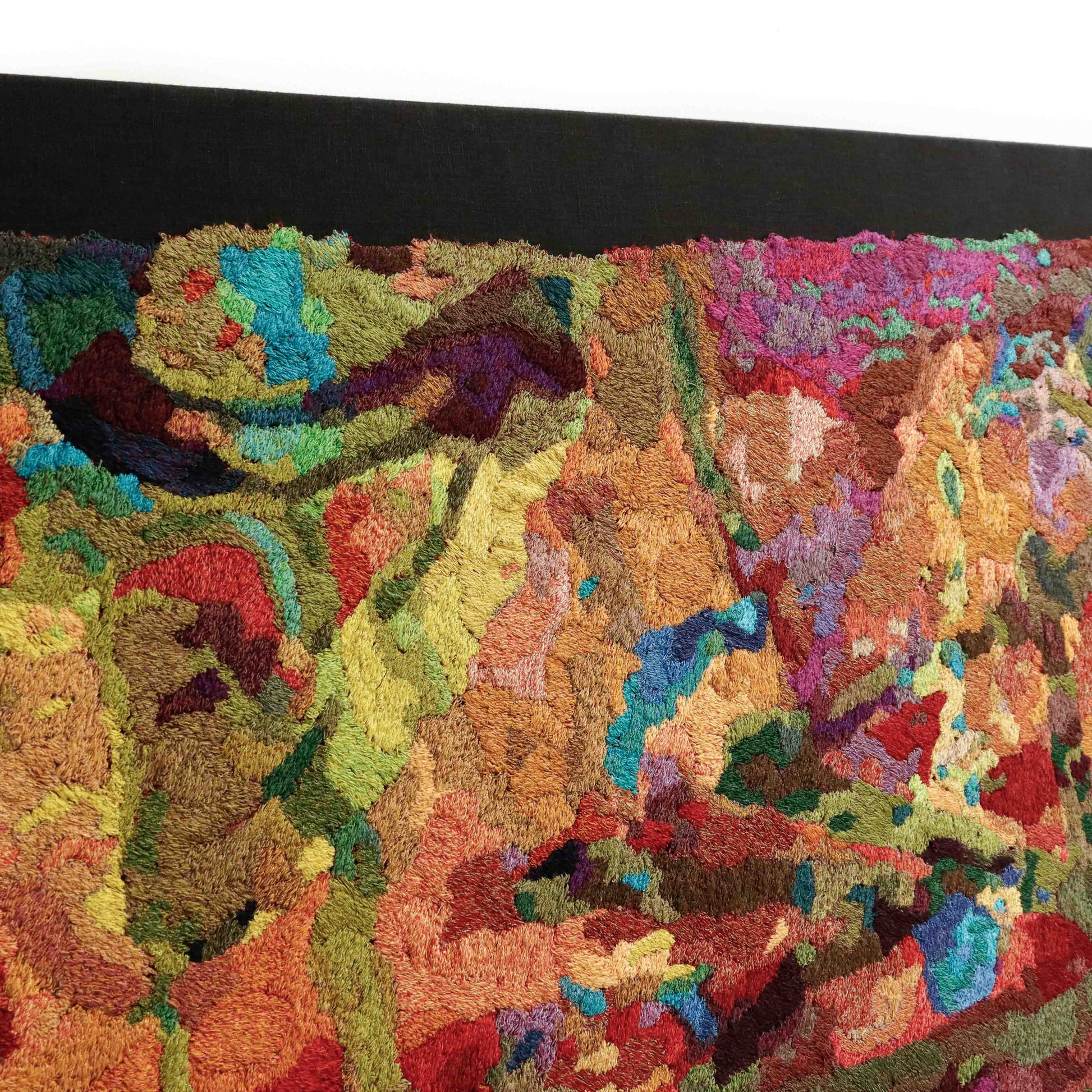 Angled view of a framed thread tapestry, showcasing dense, colorful thread stitching in an abstract embroidery design.