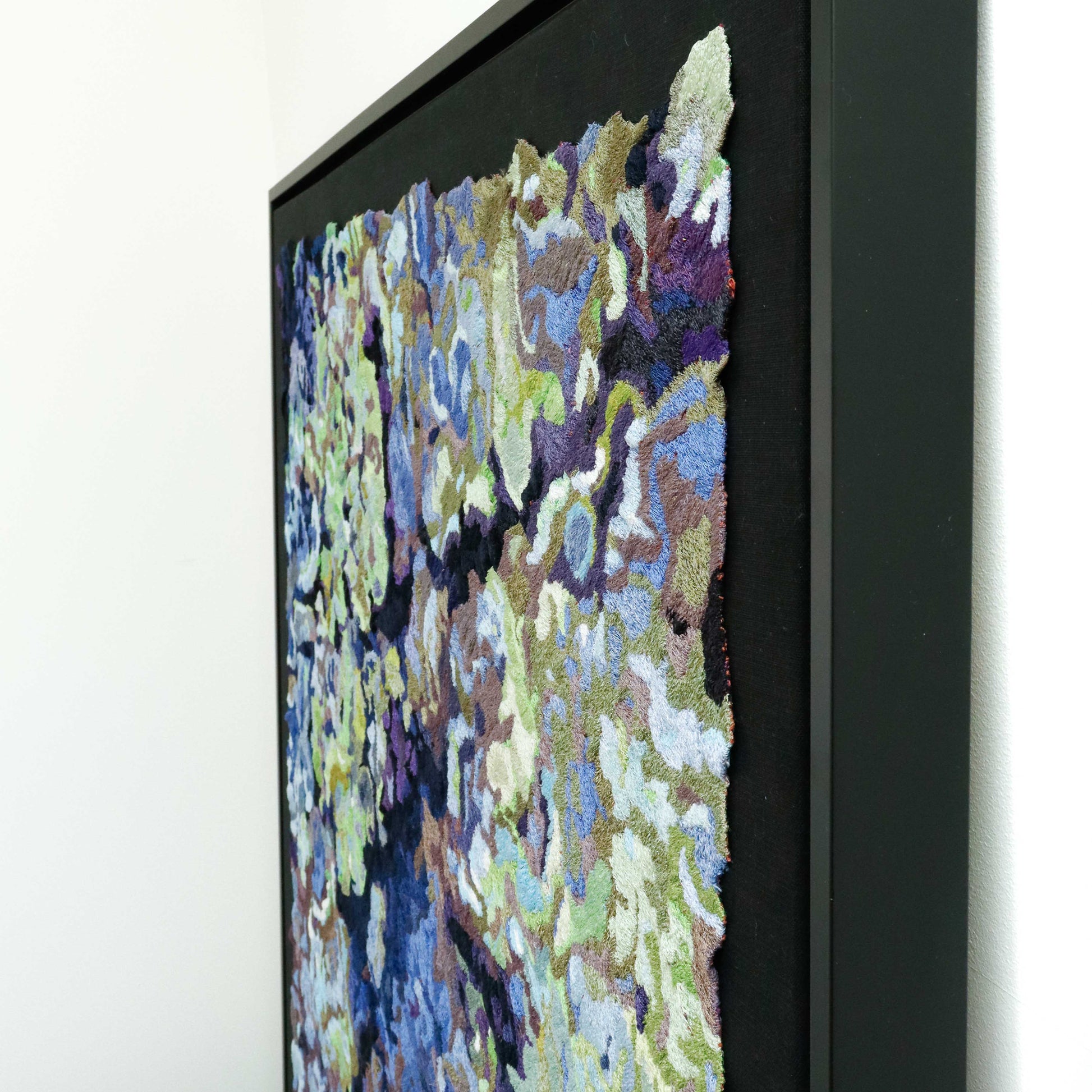 A framed thread painting, viewed from the side, showcasing intricate stitching and colorful thread in an abstract thread painting.