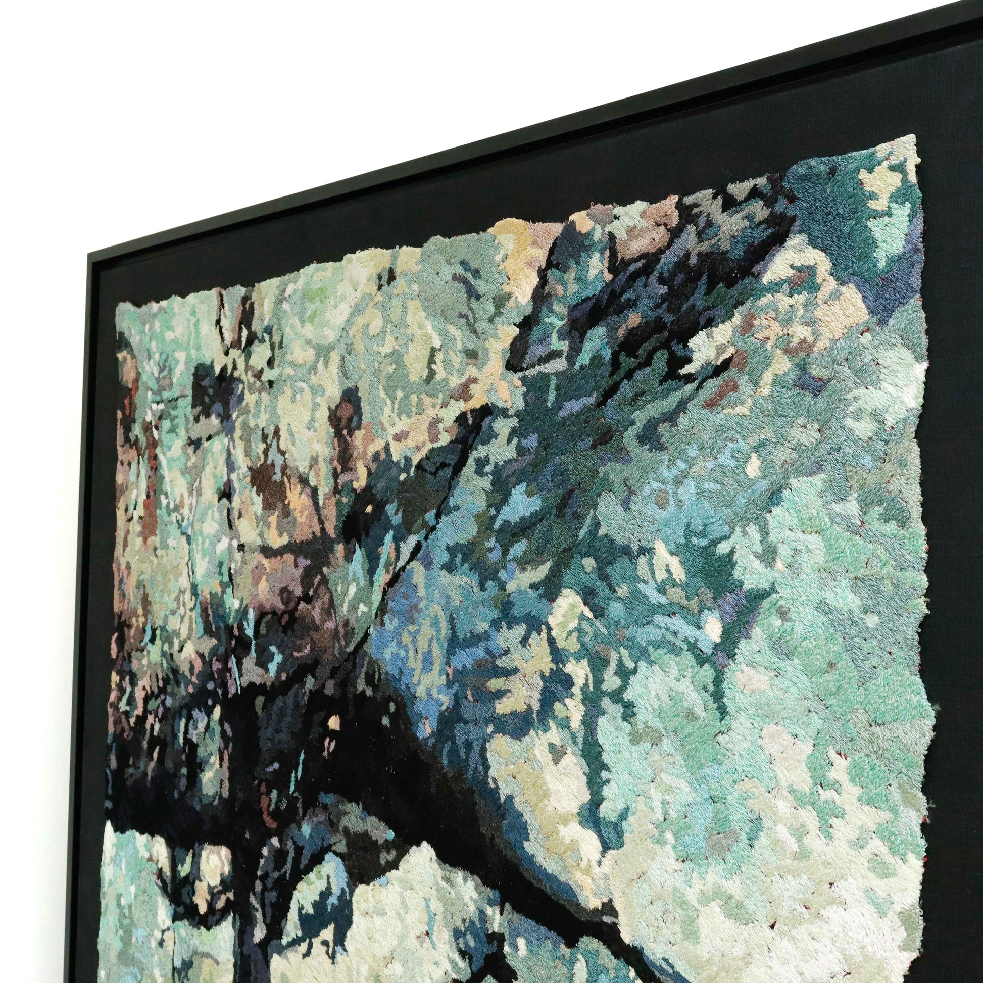 A framed thread tapestry, viewed from the side, showcasing intricate stitching and colorful thread in a stone-like thread painting. 