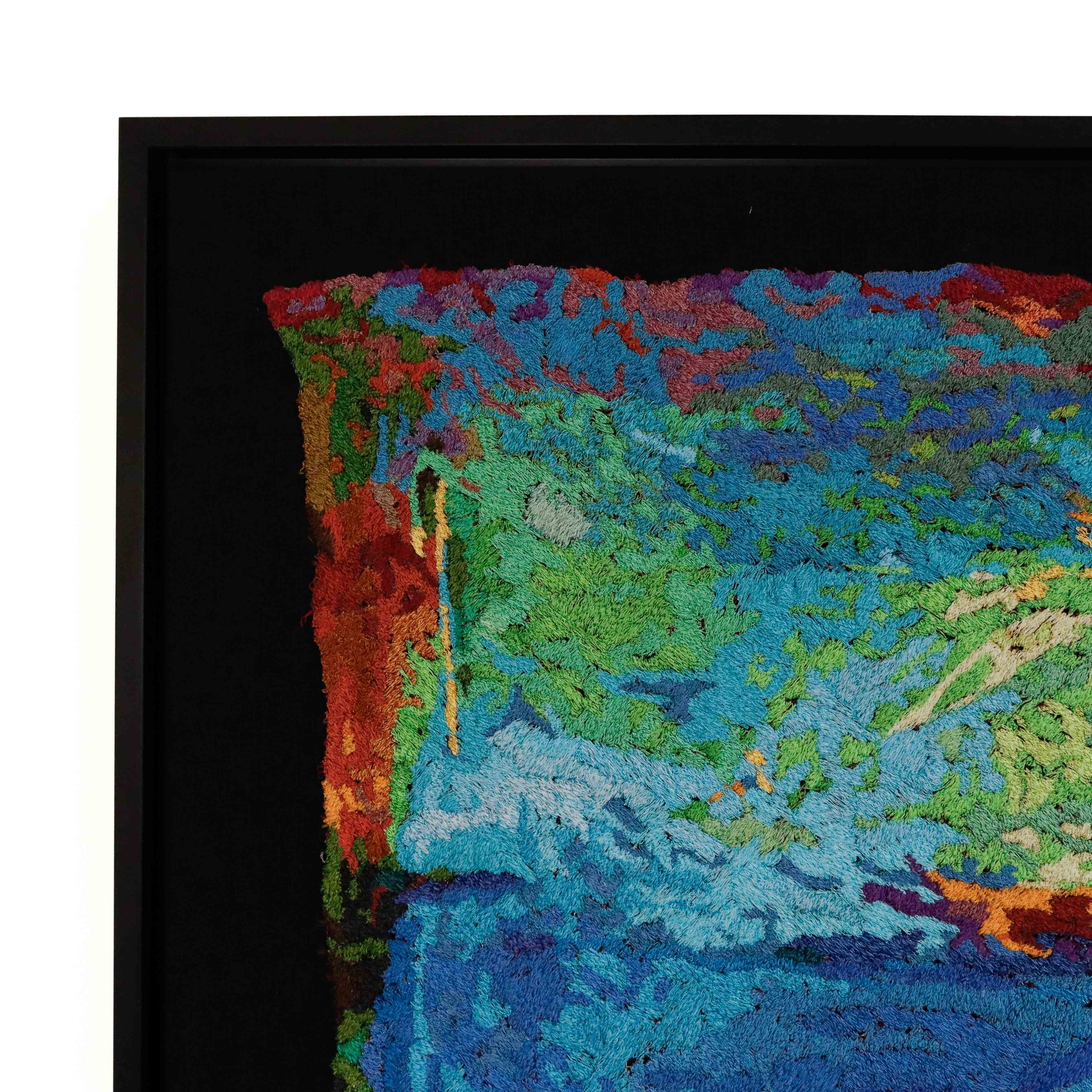 A framed thread painting, viewed from the side, showcasing intricate stitching and colorful thread in a landscape thread painting. 