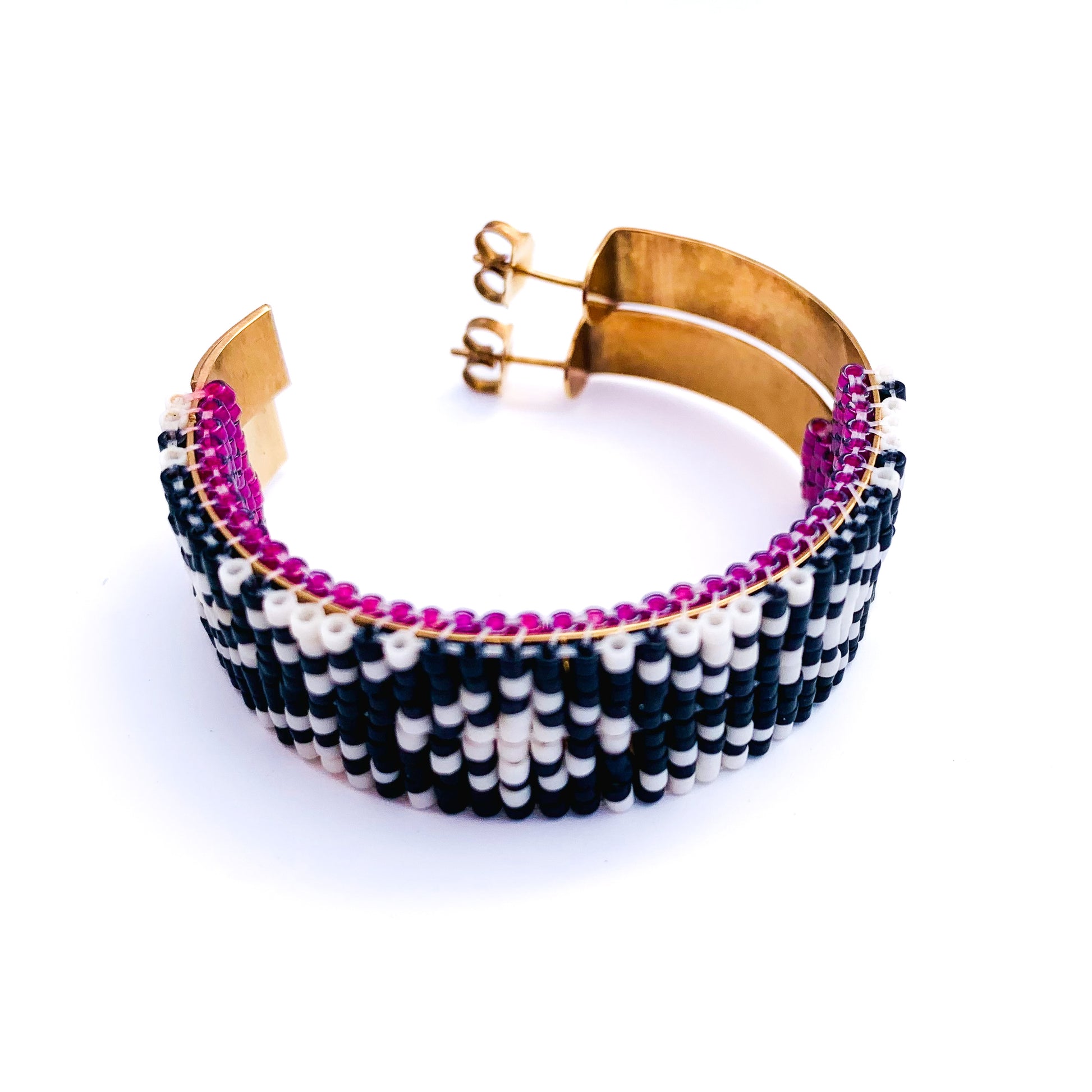 A gold hoop earring is partially covered with intricate black and white beadwork and a vibrant purple lining.