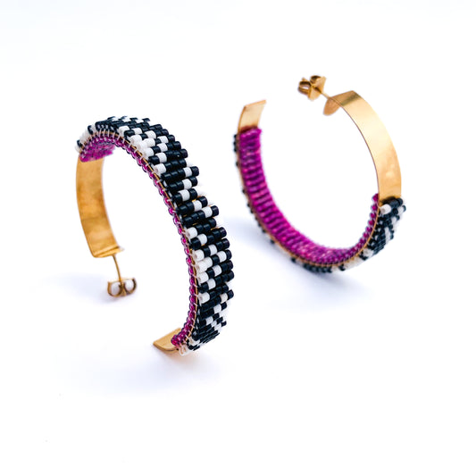 Two gold hoop earrings are partially covered with intricate black and white beadwork and a vibrant purple lining.