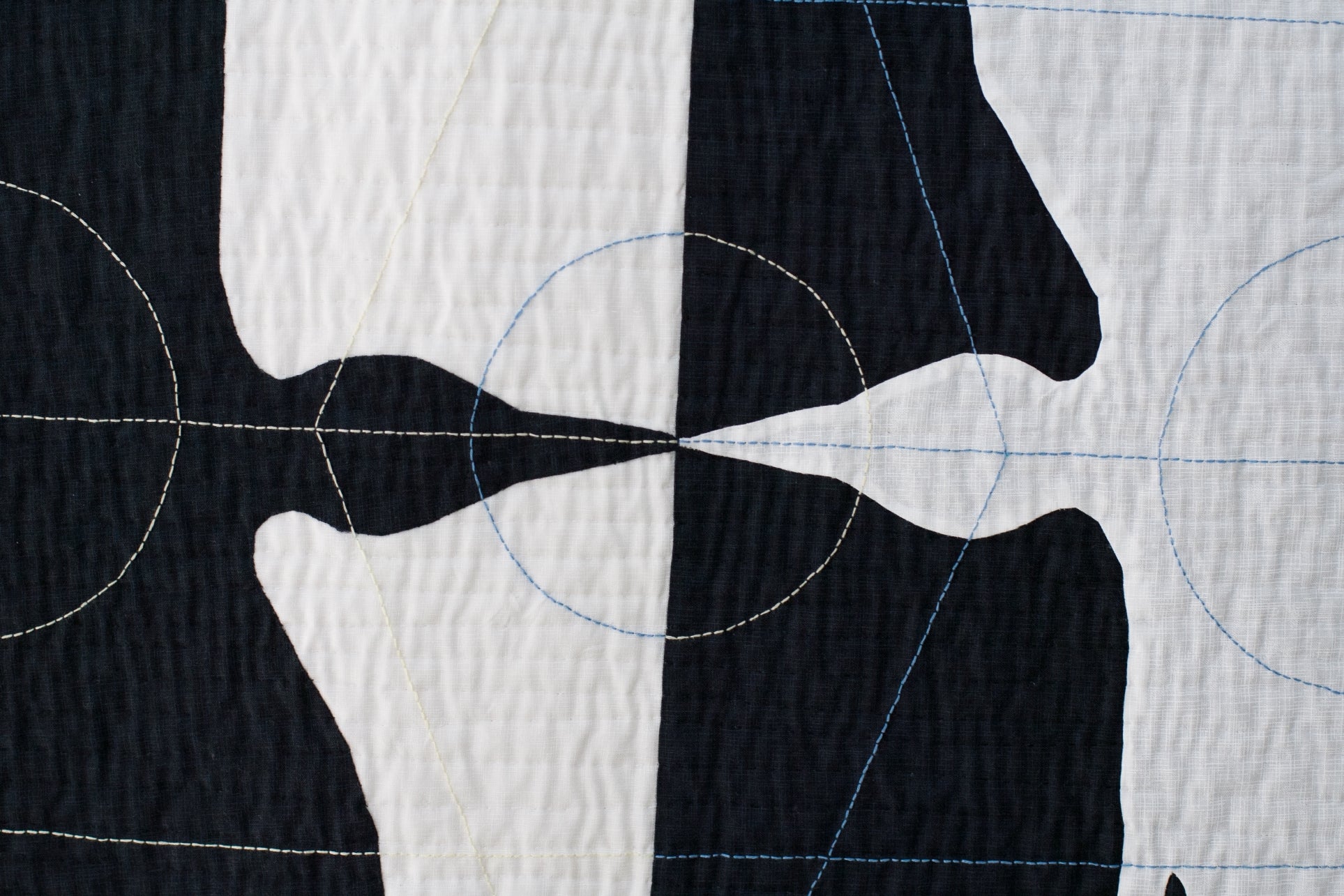 Close-up of textile art: contrasting bird silhouettes with circular and linear stitching details on textured fabric.