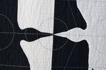 Close-up of textile art: contrasting bird silhouettes with circular and linear stitching details on textured fabric.