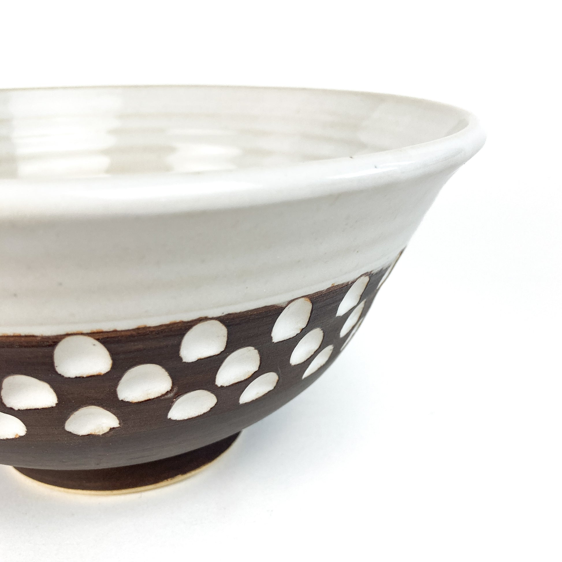 A close-up of a two-toned bowl with a white rim and brown base featuring white carved details.