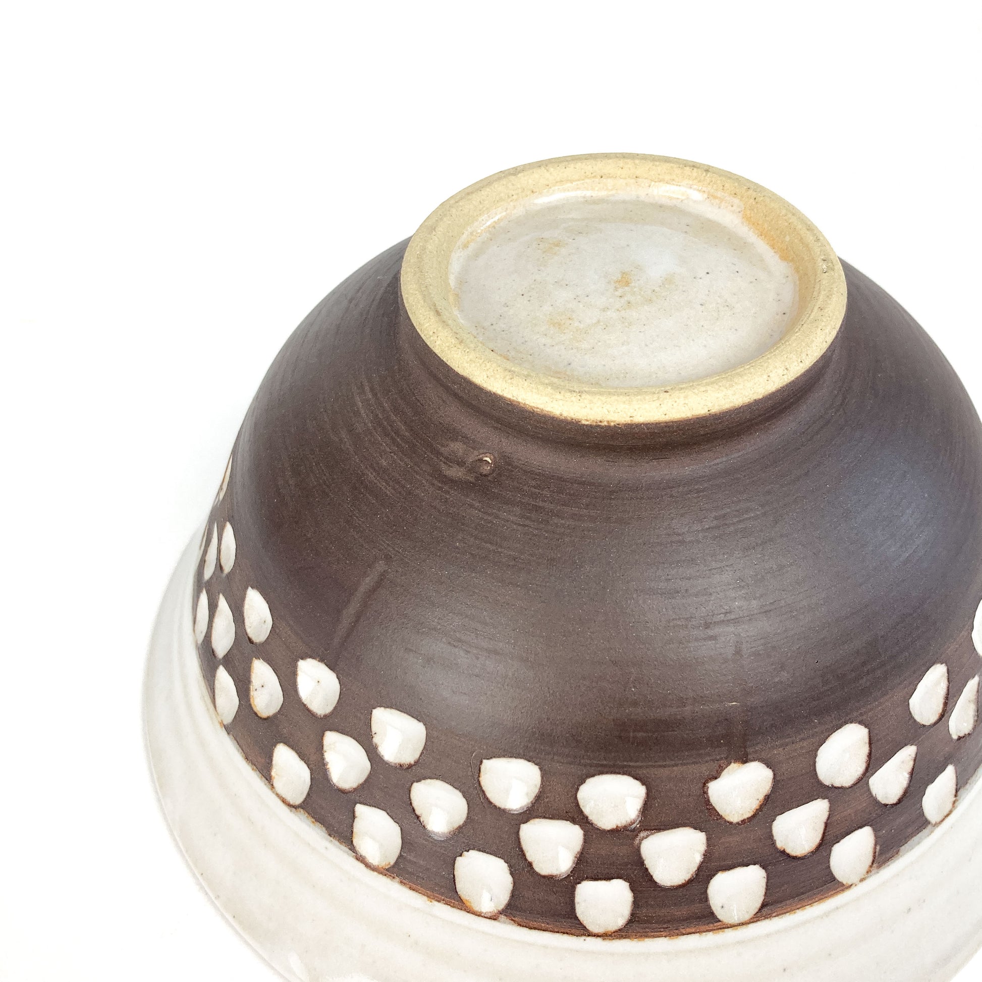 A close-up of the bottom of a two-toned bowl with a white rim and brown base featuring white carved details.