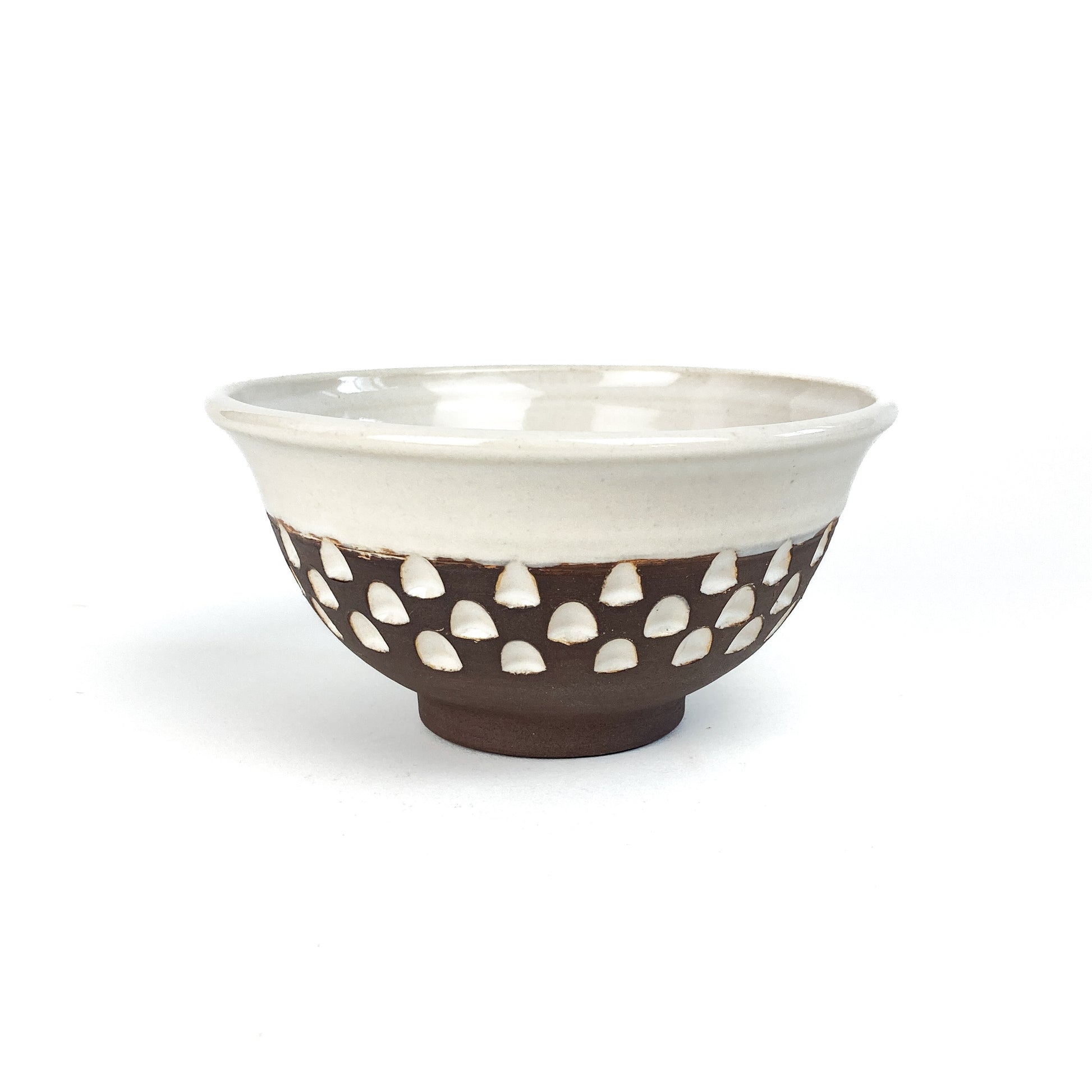 A two-toned bowl with a white rim and brown base featuring white carved details.