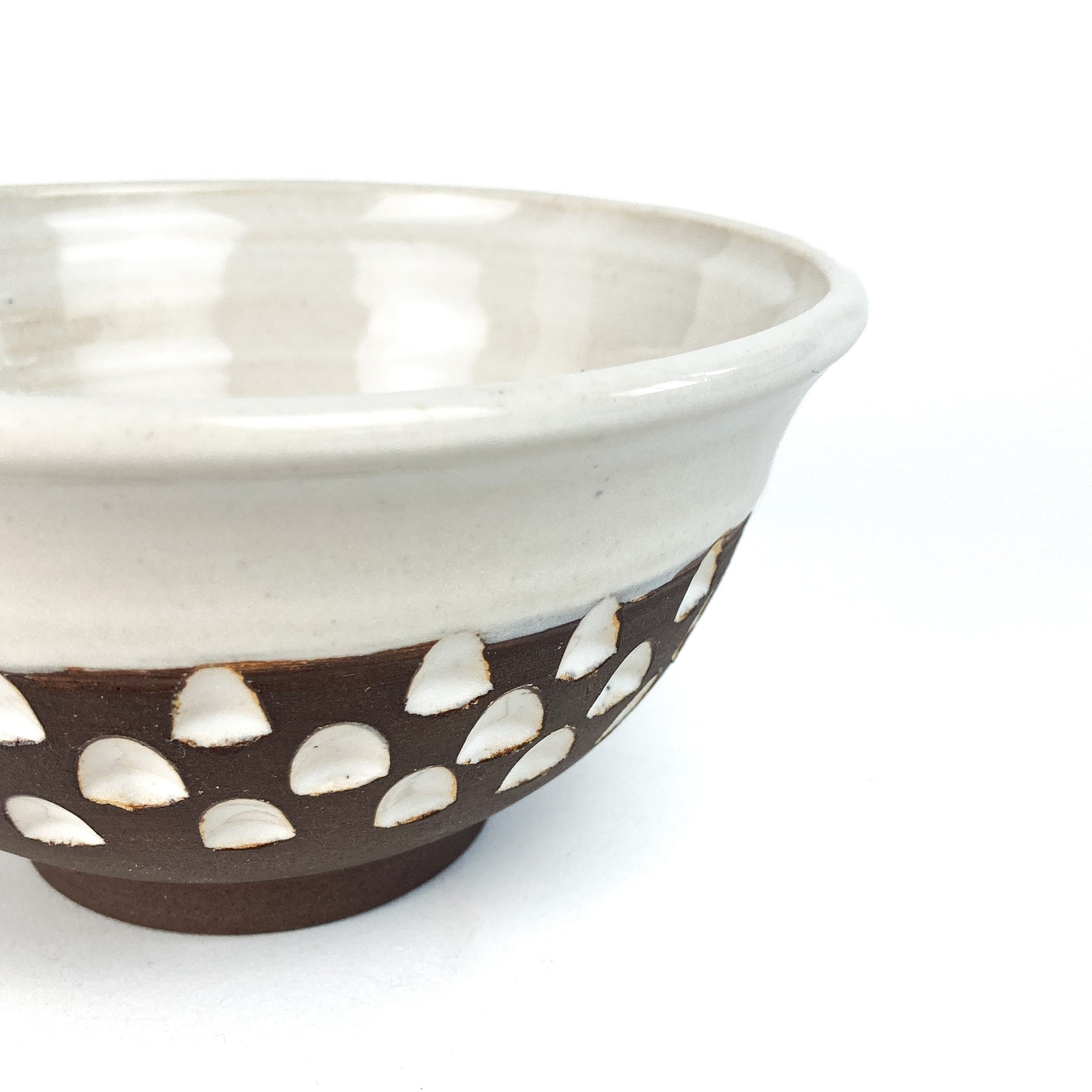 A close-up of a two-toned bowl with a white rim and brown base featuring white carved details.