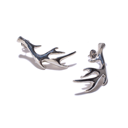 Two shiny silver stud earrings shaped like stylized deer antlers are displayed.