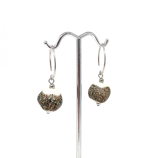 A pair of earrings with speckled glass beads with white tops hanging from silver hoops on a metal stand.