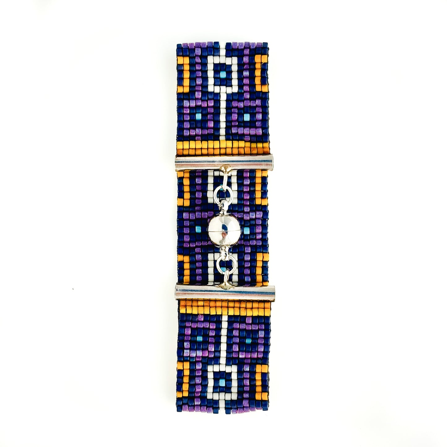A flat lay shows a beaded bracelet with a geometric design in purple, blue, orange, and white and a silver magnetic clasp.