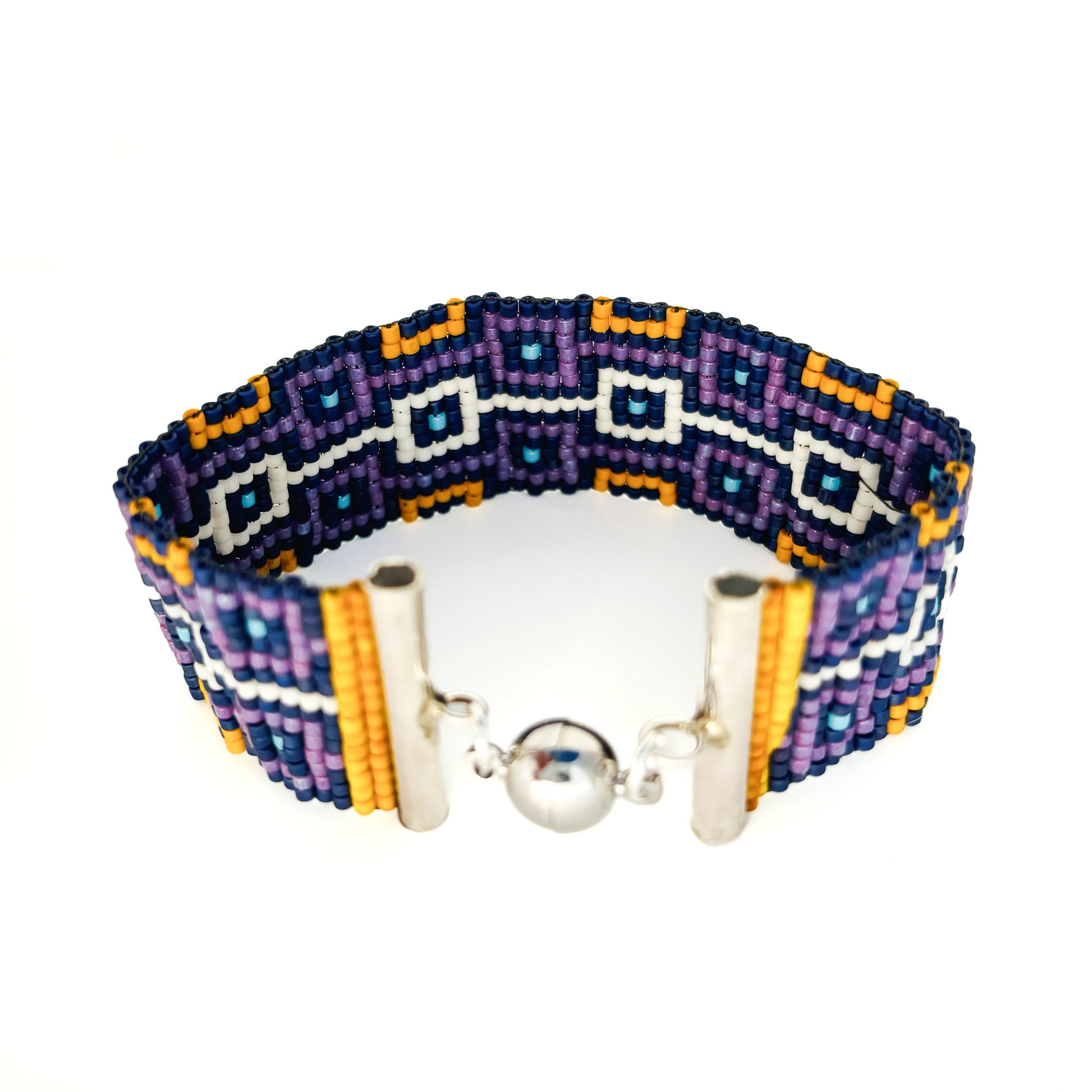 A beaded bracelet with a geometric pattern in purple, blue, orange, and white features a silver magnetic clasp.
