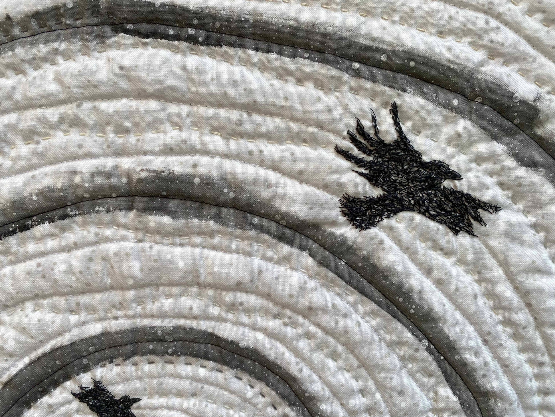 Close-up of textile art: swirling lines with a textured surface and a detailed stitched bird.