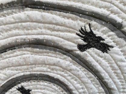Close-up of textile art: swirling lines with a textured surface and a detailed stitched bird.