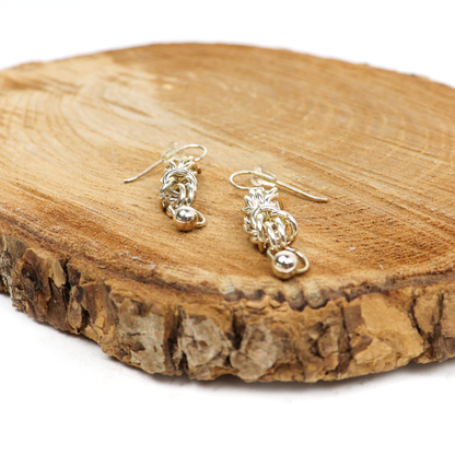 King Chain Dangle Earrings displayed on a wooden surface, showcasing silver weave and ball accents.
