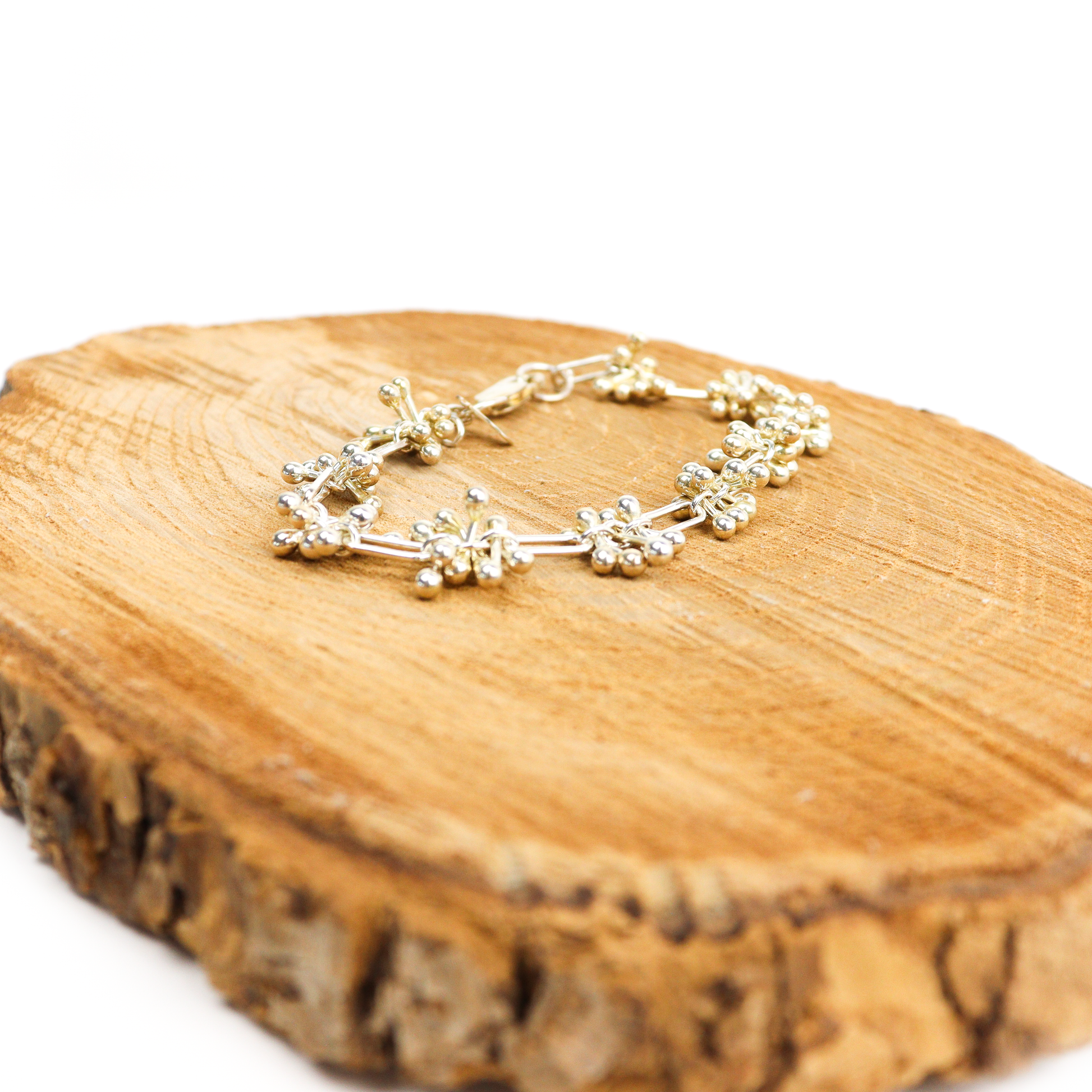 Spaced Barbell Bracelet displayed on a wooden surface, showing silver ball clusters and bar connections.