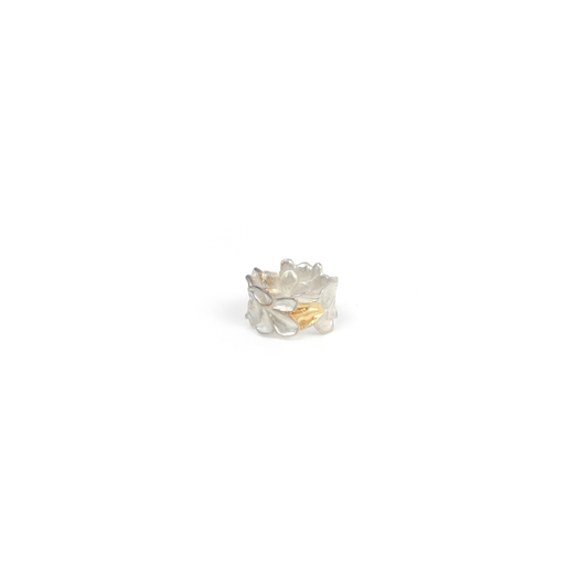 A textured silver ring with abstract, overlapping petal-like shapes and a single, contrasting gold-toned element.