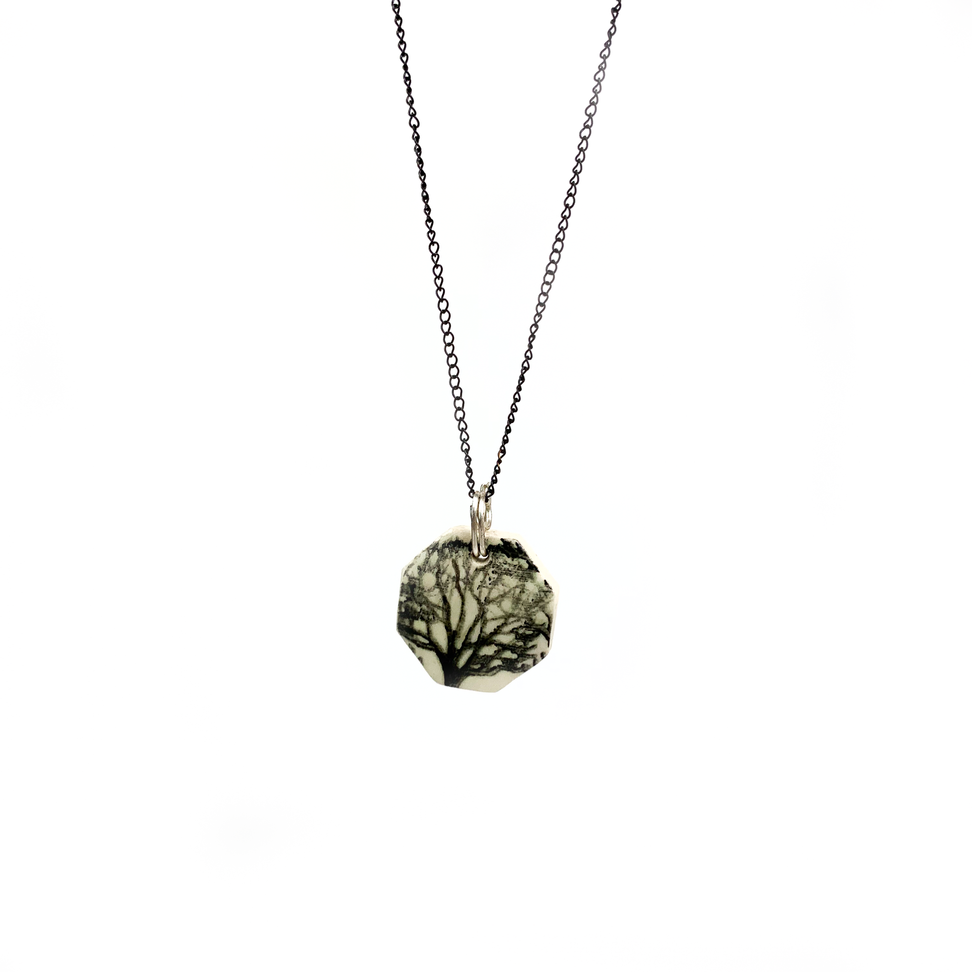 A round pendant necklace with a tree design, hanging on a thin, dark chain.