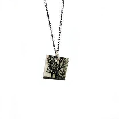 A square pendant necklace with a tree design, hanging on a thin, dark chain.