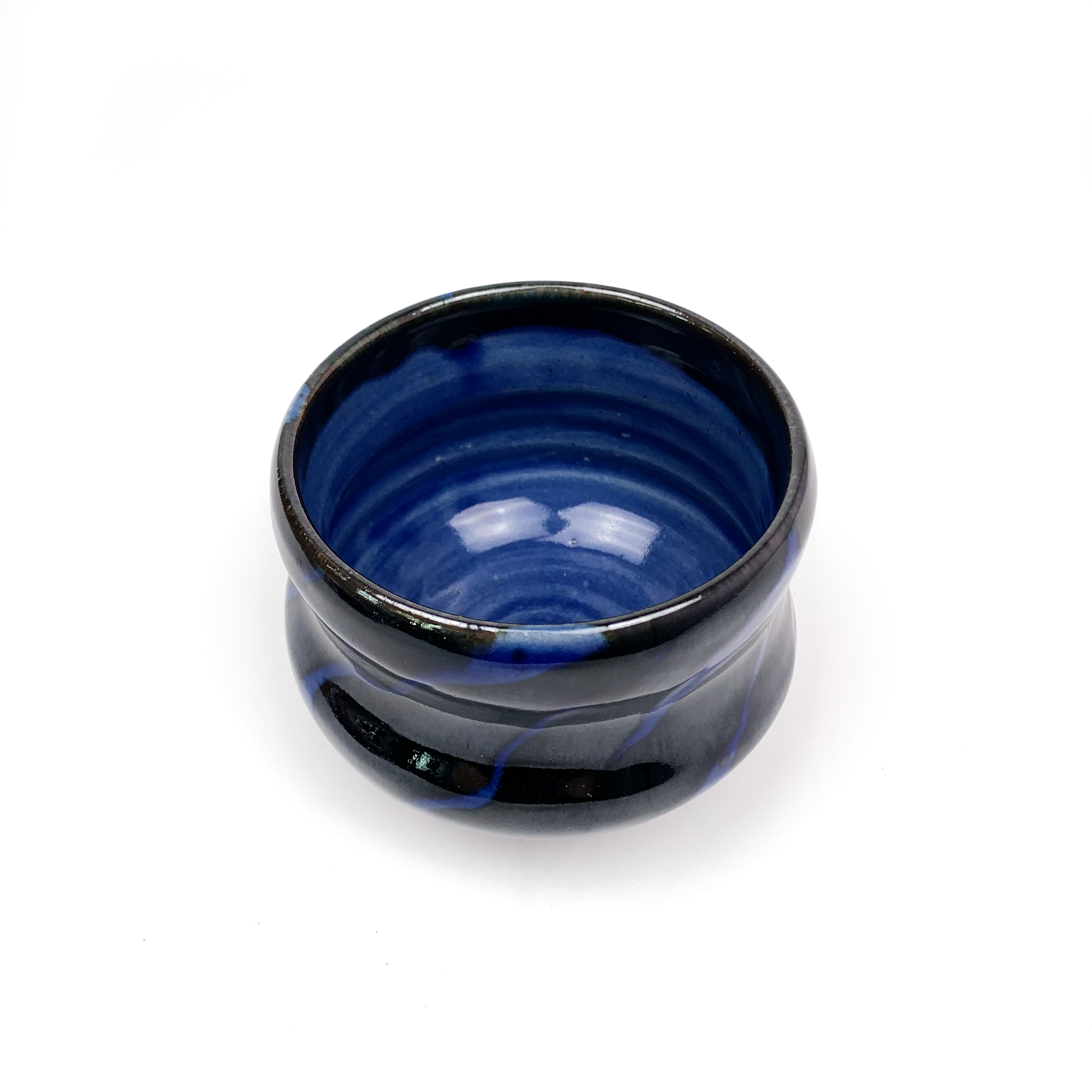 A dark ceramic tea bowl with blue swirls, viewed from above.