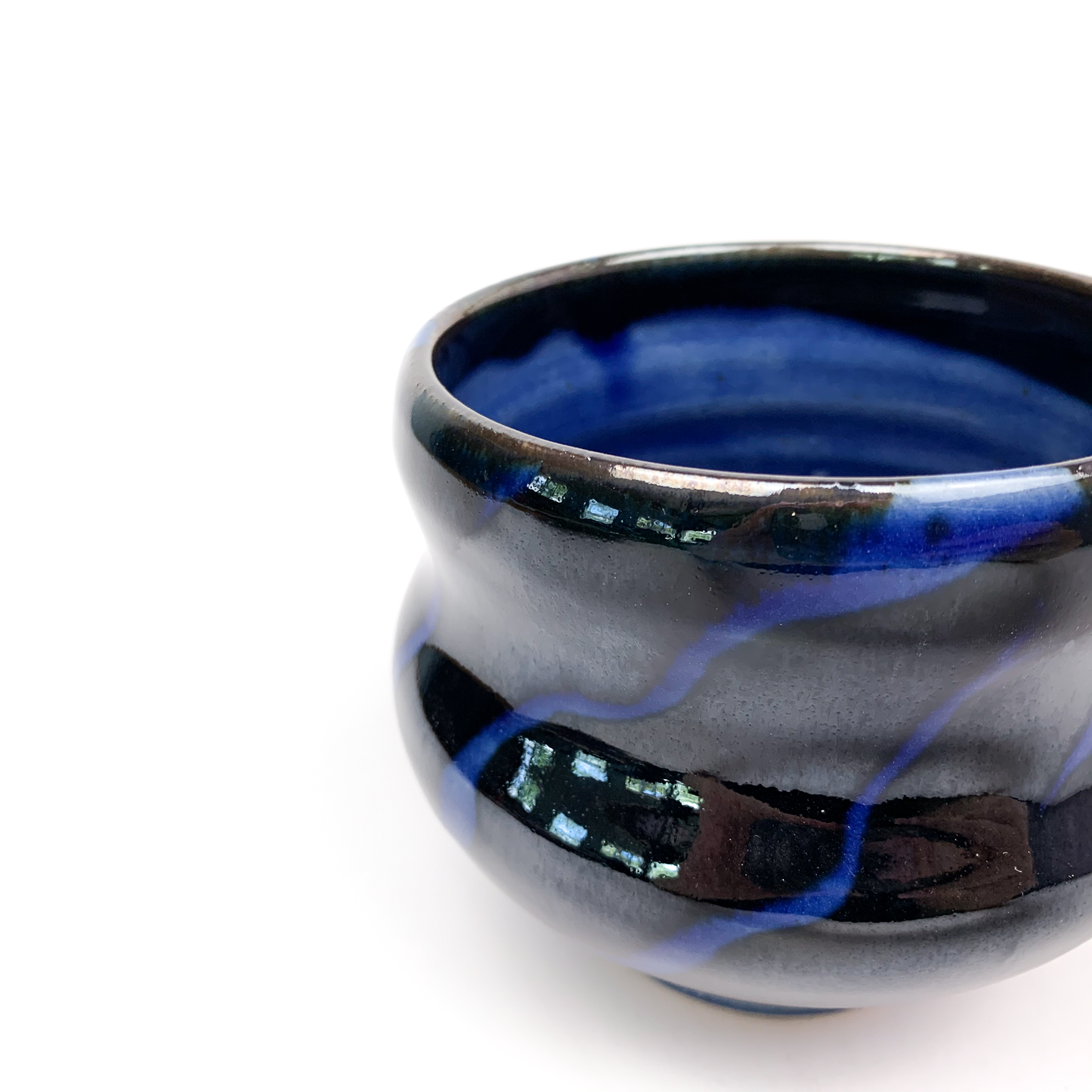 A close-up of a dark ceramic tea bowl with blue swirls.