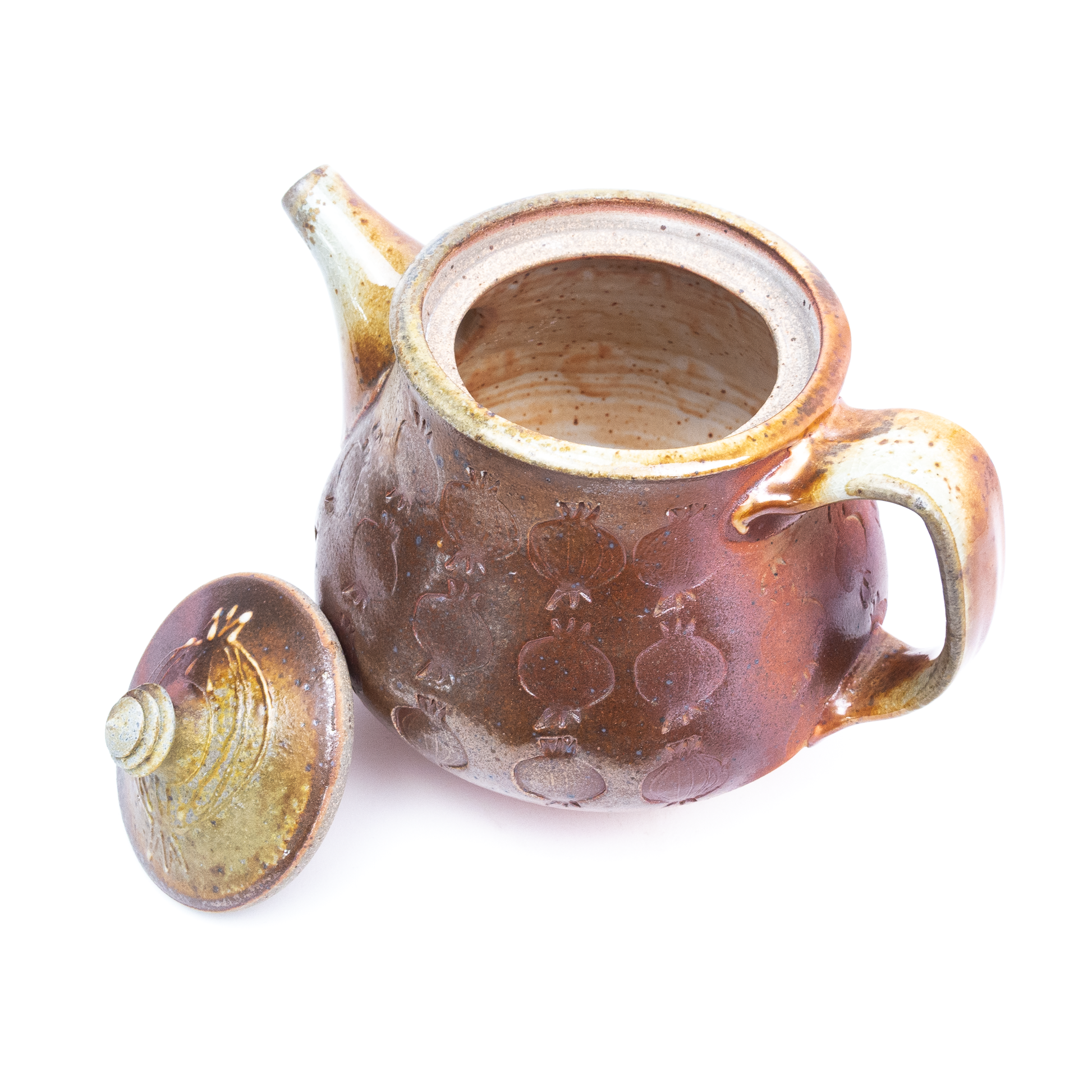 A wood-fired ceramic teapot with its lid removed reveals its interior and the impressed pomegranate pattern on its exterior.