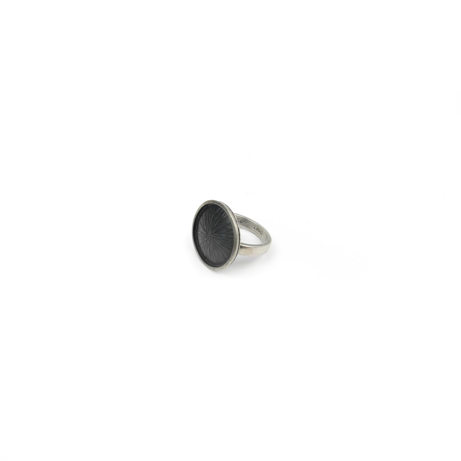 Silver ring with a large, round, dark textured face featuring a radiating design. Inscriptions "925" and "DMT" are visible on the band.