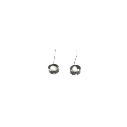 Two silver earrings with baroque pearls nestled in textured circular settings hang from silver hooks.