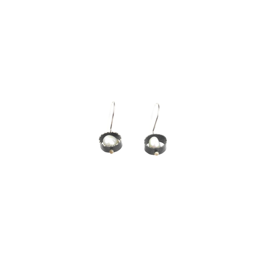 Two silver earrings with baroque pearls nestled in textured circular settings hang from silver hooks.