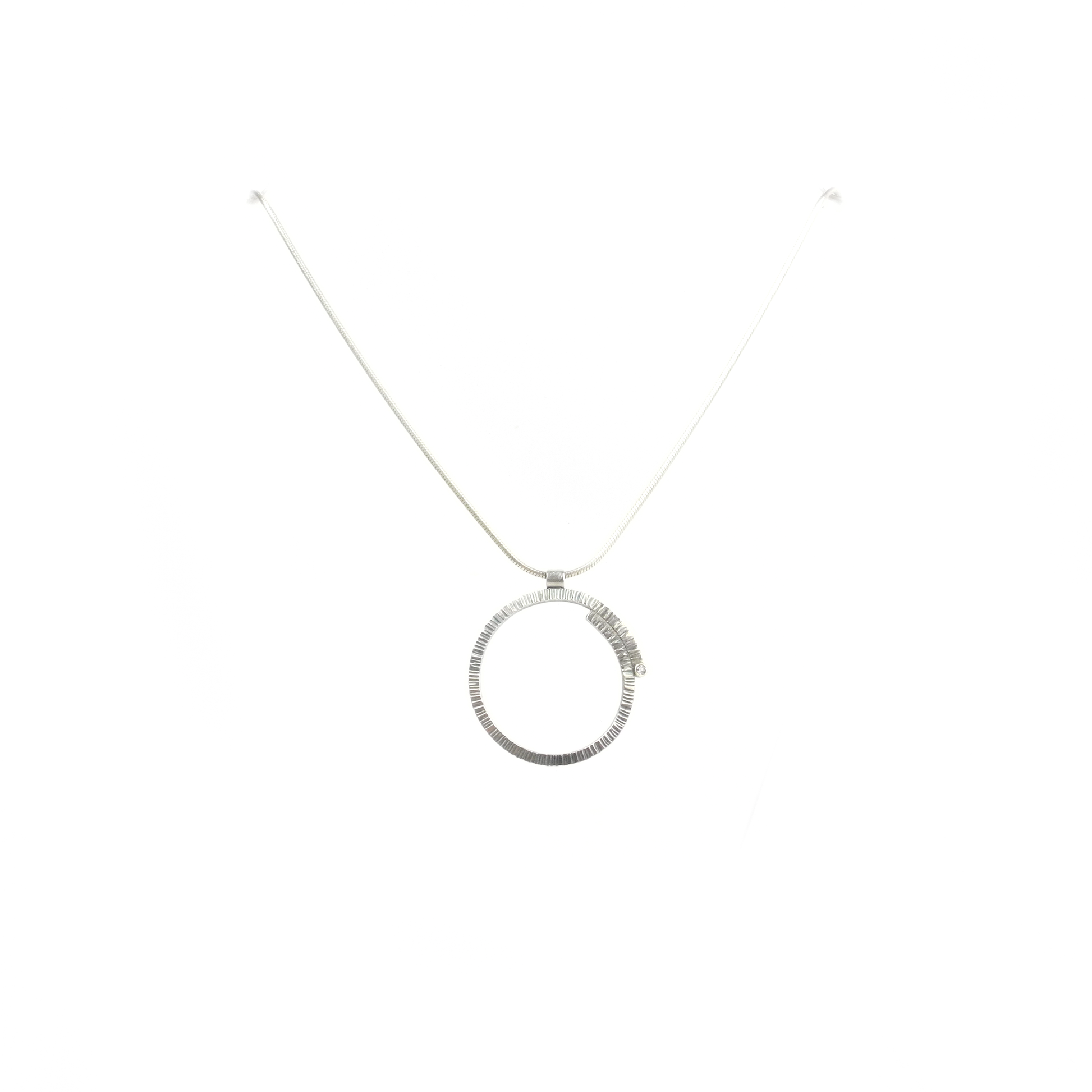 A metallic pendant with a textured circular design hangs from a delicate chain.