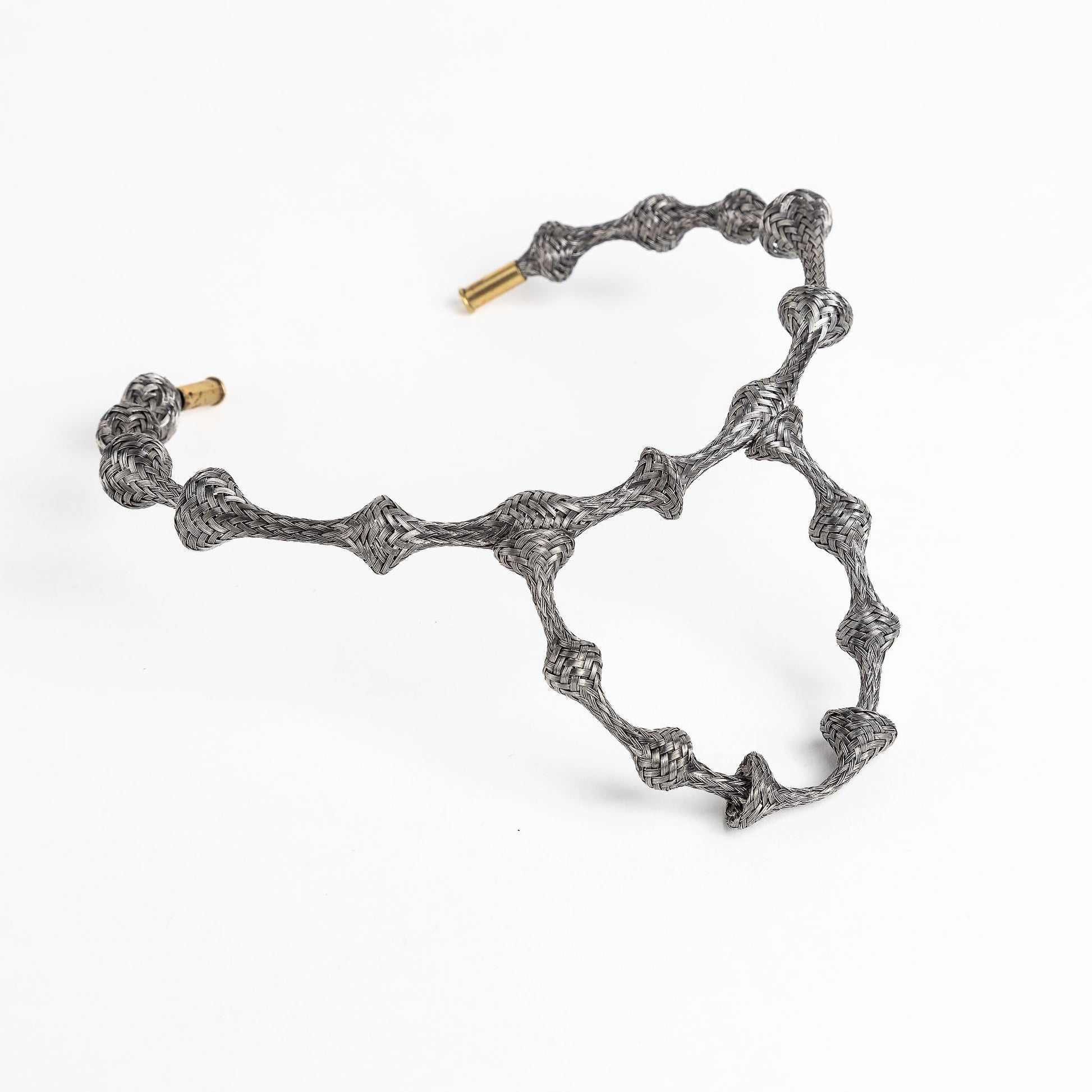 Braided stainless steel cuff bracelet with gold end caps, curved in a heart shape, on white.