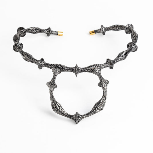 Braided stainless steel cuff bracelet with gold end caps, curved in a heart shape, on white.
