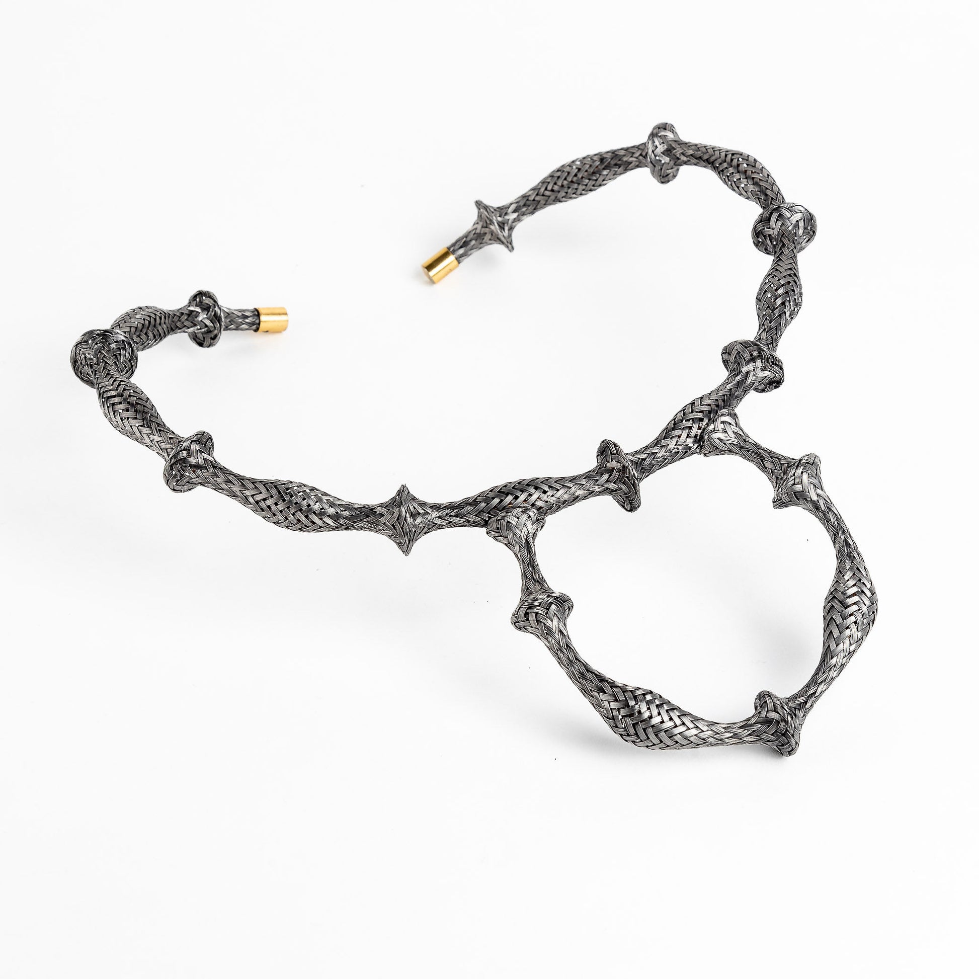 Braided stainless steel cuff bracelet with gold end caps, curved in a heart shape, on white.