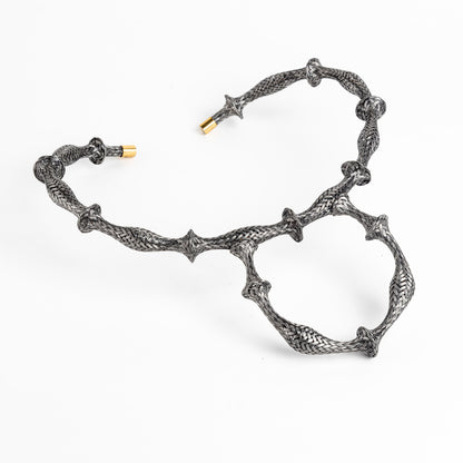 Braided stainless steel cuff bracelet with gold end caps, curved in a heart shape, on white.