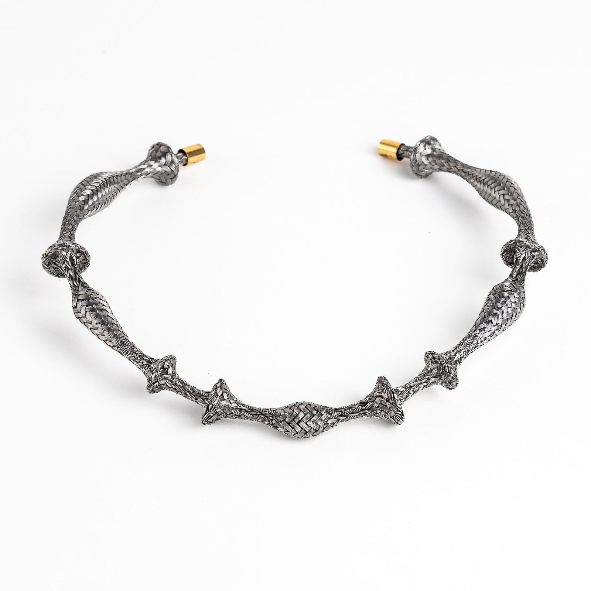 Braided stainless steel cuff bracelet with gold end caps, curved, on a white background.