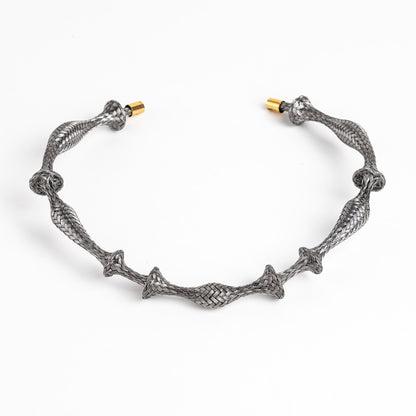 Braided stainless steel cuff bracelet with gold end caps, curved, on a white background.