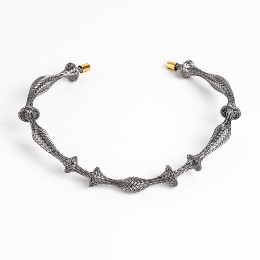 Braided stainless steel cuff bracelet with gold end caps, curved, on a white background.