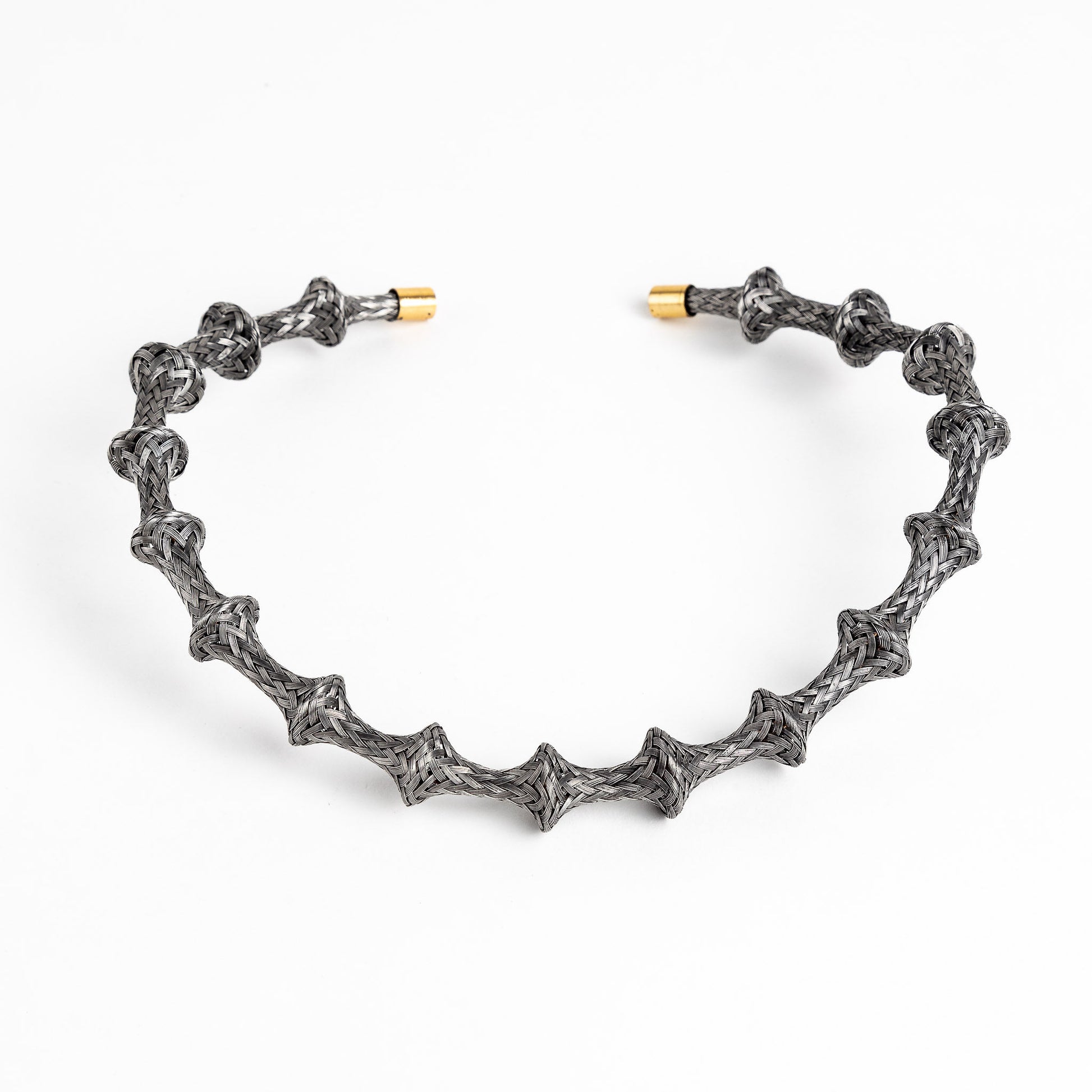 Braided stainless steel cuff bracelet with gold end caps, curved, on a white background.