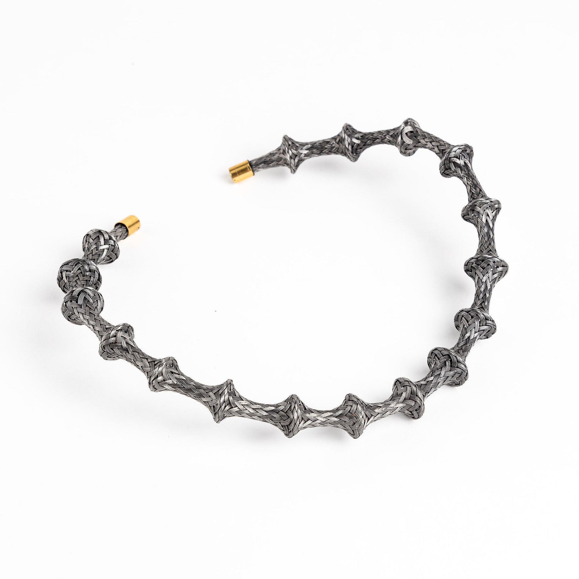 Braided stainless steel cuff bracelet with gold end caps, curved, on a white background.